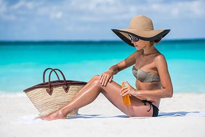 woman on beach putting on lotion wearing a large brim hat